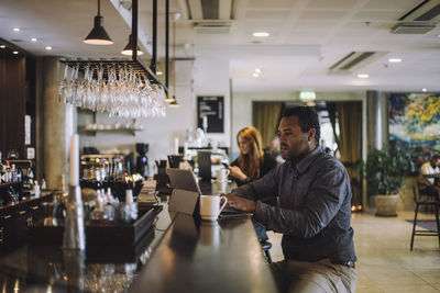 Male freelance worker using laptop while sitting at bar counter in restaurant