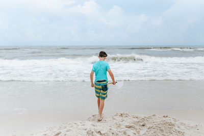 Full length of boy standing at beach against sky