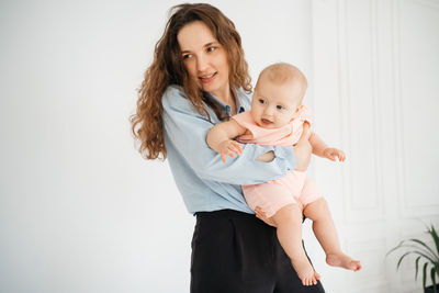 Young mother with long hair and in a shirt holds a newborn daughter. 