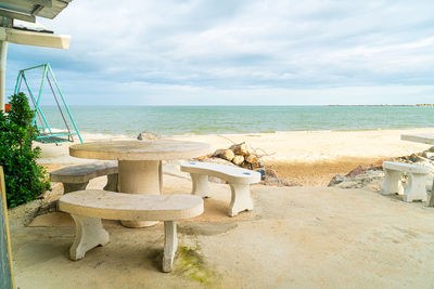 Chairs and table on beach against sky