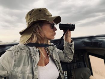 Woman looking through binoculars while sitting in safari vehicle at national park