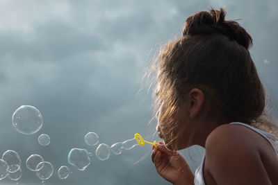 Close-up of girl blowing on bubble wand against sky