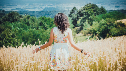 Rear view of young woman standing on field during sunny day