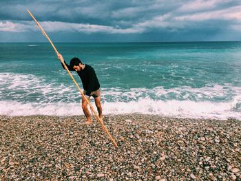 Fisherman with pole on seashore against cloudy sky