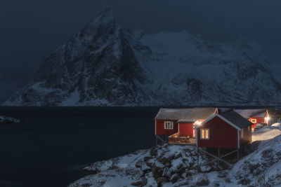 House amidst snow covered houses and mountains against sky at night