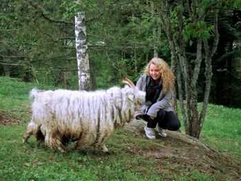 Young woman crouching by sheep on grassy field
