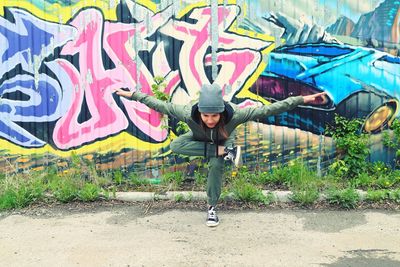 Young woman with arms outstretched standing on road against wall