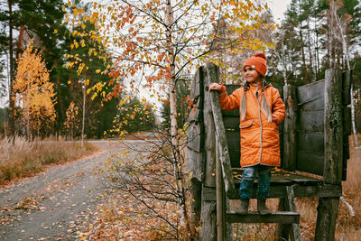 Happy girl in orange coat walks and plays in handmade wooden house in autumn park. active weekend