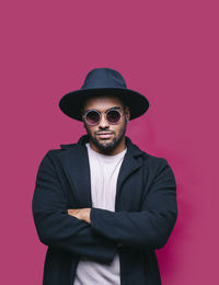 Portrait of man wearing sunglasses standing against red background