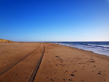 Tire tracks at sandy beach against blue sky