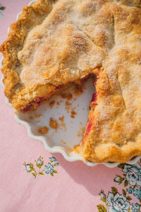 Whole rhubarb pie with missing slice, pink tablecloth with blue roses