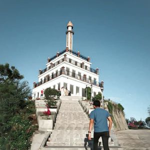 Rear view of man standing by building against sky