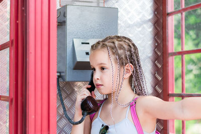 A serious girl with afro-braids makes a phone call in an old english telephone booth