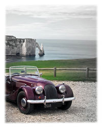 Vintage car on land by sea against sky