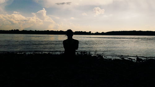 Rear view of silhouette woman standing by lake against sky