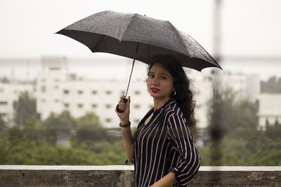 Portrait of woman with umbrella standing in rain during rainy season