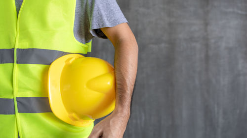 Midsection of man holding yellow while standing against wall