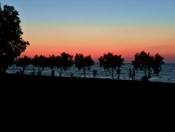 Silhouette trees by lake against sky during sunset