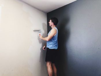 Side view of young man standing against wall at home