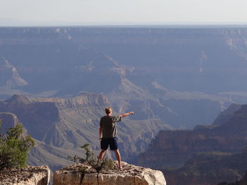 Rear view of man standing on rock while looking at mountains