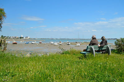 Rear view of people sitting by sea on bench