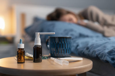 Close-up of medicine while sick woman resting in background