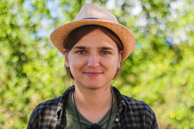 Close-up light smiling young brunette caucasian woman in hat. summer blurred green nature bokeh