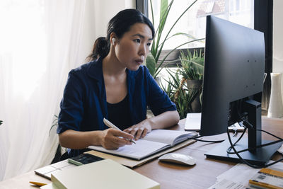 Confident female architect with diary looking at computer monitor on desk in home office