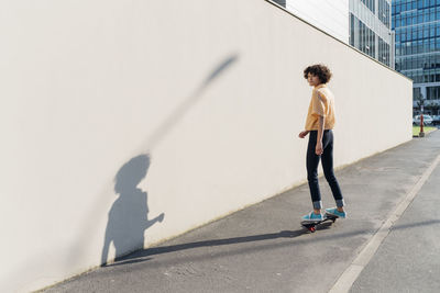 Woman skateboarding on footpath by wall on sunny day