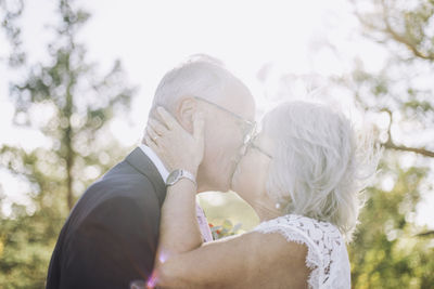 Romantic newlywed senior bride kissing groom on mouth at wedding during sunny day