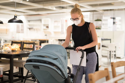 Woman wearing flu mask holding stroller at store