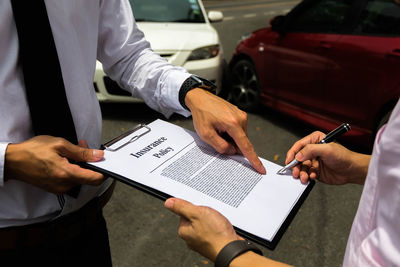 Midsection of insurance agent pointing while costumer signing contract outdoors