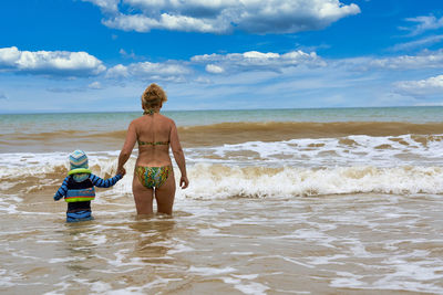 Rear view of shirtless boy on beach against sky