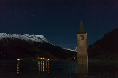 Illuminated building by lake against sky at night