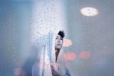 Thoughtful man seen through wet glass window