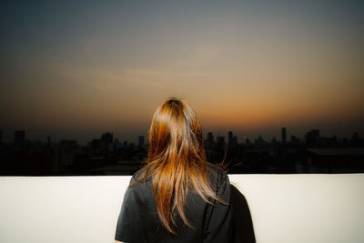 Rear view of woman looking at cityscape against sky