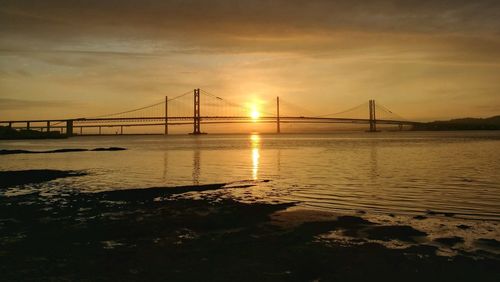 Suspension bridge over sea during sunset