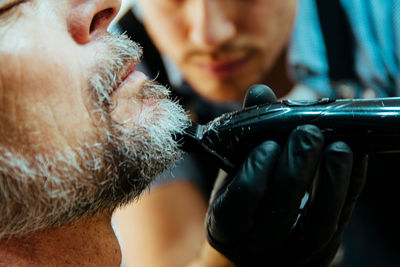 Close-up of barber trimming beard of man at salon