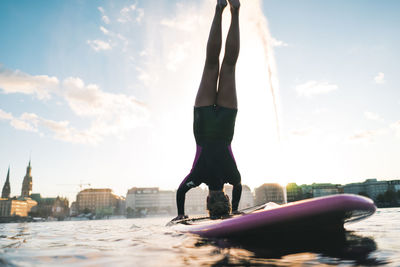 Midsection of woman with arms outstretched against sky in city