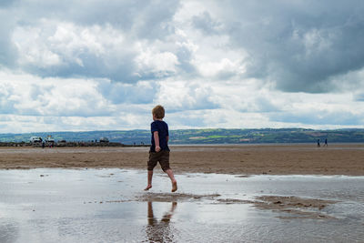 Boy walking on beach against sky