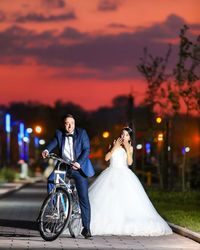 Young couple with umbrella against sky during sunset