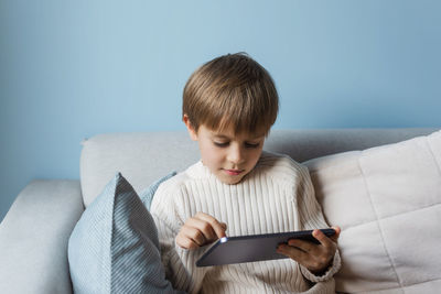 Boy is relaxing on the sofa at home and using a tablet.