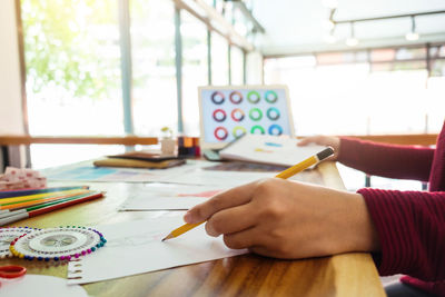 Cropped hand of fashion designer sketching on desk in office