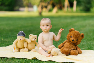 A baby sitting on a blanket outdoors, smiling and playing with teddy bears, enjoying a lively moment 