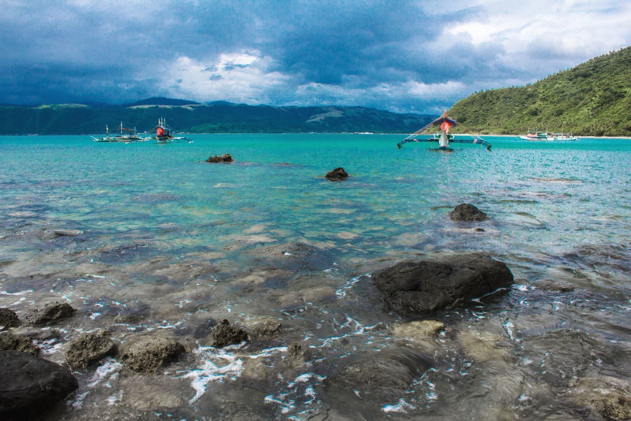 water, sky, sea, cloud - sky, rock, nature, nautical vessel, solid, beauty in nature, day, scenics - nature, transportation, rock - object, tranquil scene, mountain, tranquility, waterfront, land, mode of transportation, outdoors, sailboat, turquoise colored, shallow