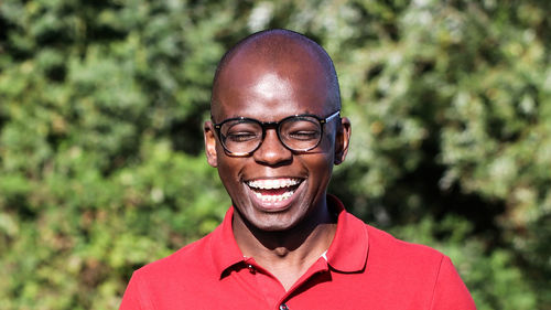 Close-up of young man wearing eyeglasses while laughing against plants