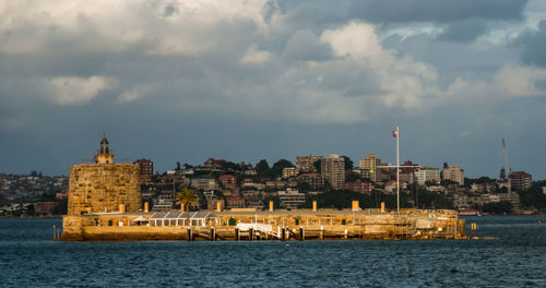 Buildings at waterfront against cloudy sky