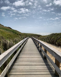 View of wooden bridge on landscape against sky