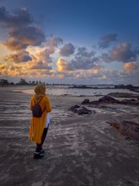 Rear view of woman standing at beach during sunset