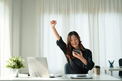 Happy businesswoman using smart phone at desk in office